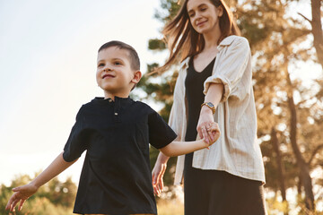 Fototapeta premium Holding each other by a hands. Mother and son are in the forest together