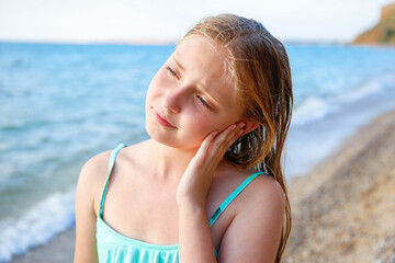 The child got water in his ear while swimming in the sea. The girl cleans her ear from water