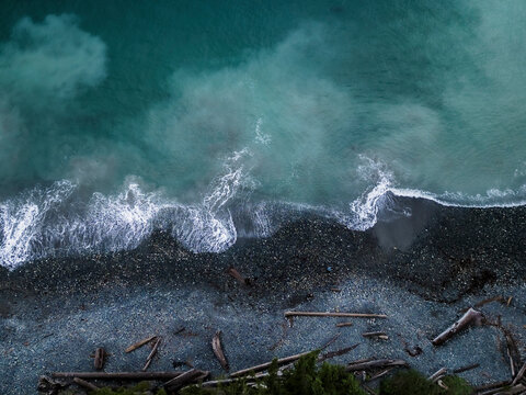 Aerial view of tranquil shoreline with logs and pebbles on rocky beach, Sooke, British Columbia, Canada.