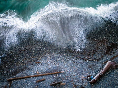 Aerial view of serene shoreline with foamy waves and driftwood, Sooke, British Columbia, Canada.