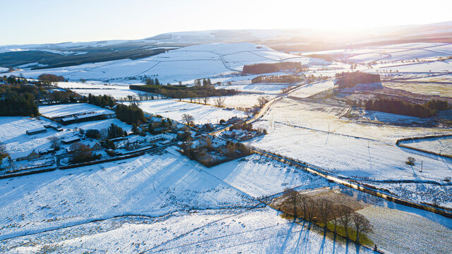 Aerial view of snowy village surrounded by mountains and fields, Chesters, Southdean, Scotland, United Kingdom.