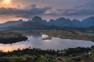 Aerial view of serene lake with majestic mountains and tranquil valley at sunset, Nashik district, Maharashtra, India.