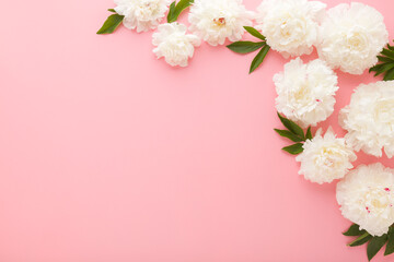 Fresh beautiful soft white peony flowers with green leaves on light pink table background. Pastel color. Closeup. Empty place for inspirational text, lovely quote or positive sayings. Top down view.