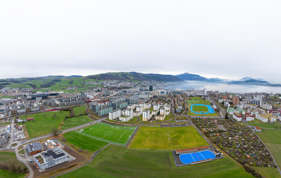 Aerial view of city, mountain, buildings, lake, sports field, and stadium in foggy Zug, Kanton Zug, Switzerland.