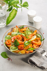 Fresh summer salad with grilled prawns, caramelized pears, cucumber and mixed greens on light grey table. Vertical image.