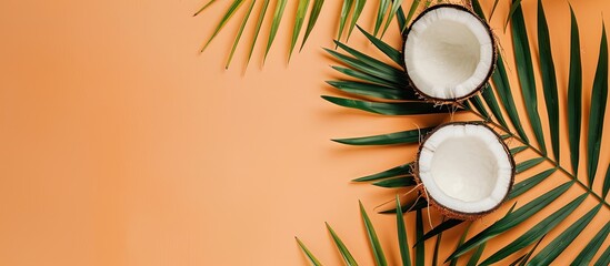 Top view of a palm leaf and coconut on a pastel orange background, ideal for a summer and tropical concept. Includes a flat lay image with ample copy space.