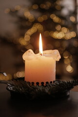 Christmas and New Year cozy  atmosphere. white candle in a black candlestick is burning against the background of blurry Christmas tree garlands. candle flame
