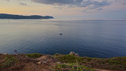 Small boat anchored on seashore in sunset at Con Son island, Vietnam. Gray background at sea, mountain, sky clouds concept.