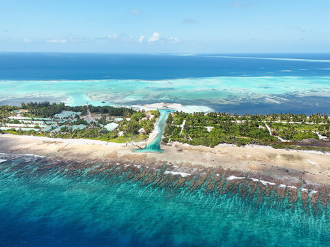 Aerial view of turquoise ocean with beach, reef, waves, and houses, Meedhoo, Addu Atoll, Maldives.