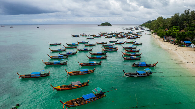 Aerial view of anchored fisherman boats on a sandy beach with turquoise ocean and tropical trees, Koh Lipe Island, Thailand.
