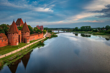 Obraz premium Castle of theTeutonic Order in Malbork by the Nogat river at sunset.