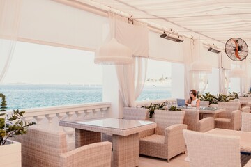 Woman coffee cafe laptop sea. Female freelancer using laptop on coffee break in modern cafe with sea view in the morning