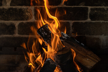 Burning logs in a fireplace with a brick wall behind it