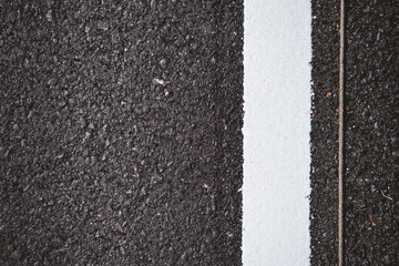 Close-up of a freshly painted white line on a black asphalt road, highlighting the texture and contrast between the two surfaces.