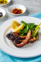 Grilled octopus with arugula and mini vegetables on a white porcelain plate