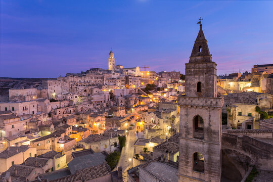 View of historic old town with illuminated buildings and church, Matera, Italy.