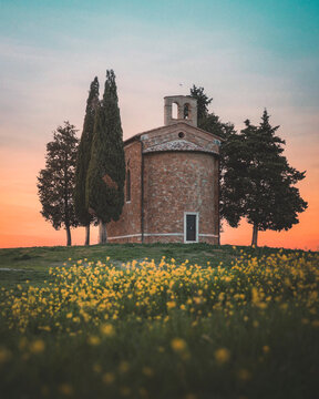 View of picturesque church, flowers, and trees during sunset in tuscany, Italy.