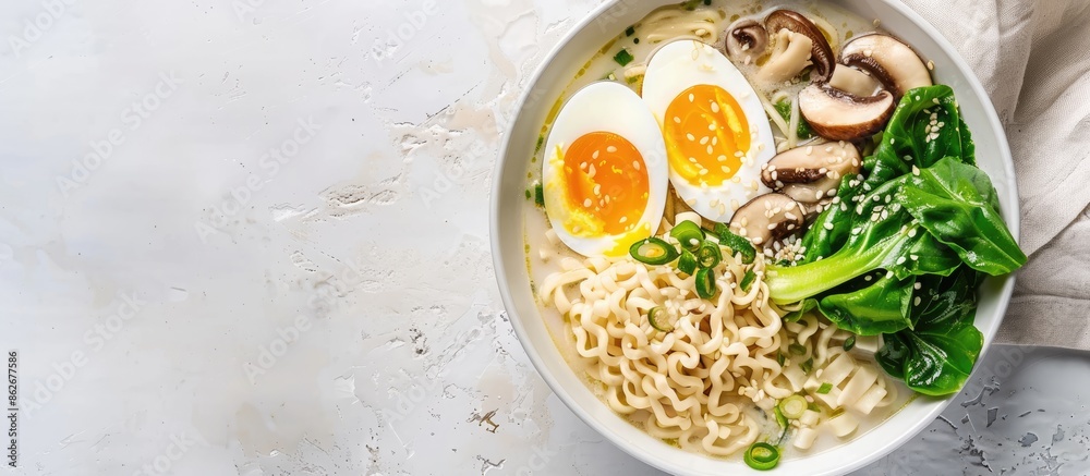 Poster top-down view of a white bowl containing ramen noodle soup with eggs, mushrooms, and pak choi on a l