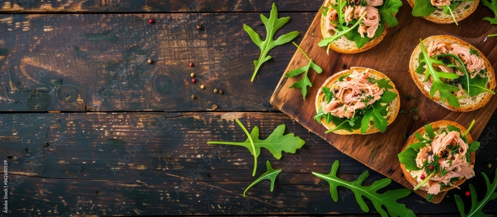 Poster top-view image of canned tuna toasts or sandwiches with lettuce and arugula on a dark wooden backdro