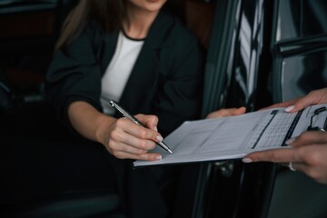 Process of buying new car, woman is signing documents while sitting in a new automobile