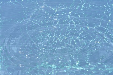 Blue water with ripples on the surface. Defocus blurred transparent blue colored clear calm water surface texture with splashes and bubbles. Water waves with shining pattern texture background.