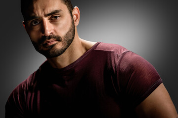 Obraz premium Portrait of strong handsome man with brutal unshaven face posing on dark background, Dark allure: Young man's serious gaze and beard create a powerful portrait against a gray background.