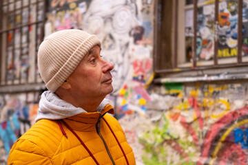 Cheerful middle-aged man, 65 in winter bright yellow puffer jacket and beanie, smiling on urban street with historic buildings in background © kittyfly