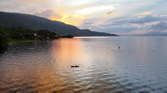 Sunset in lake toba, sumatra indonesia with a person doing kayak and a mountain in the background