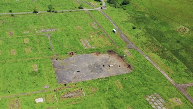 Aerial view of Stobs Camp with green fields, ruins, and winding road, Hawick, Scotland.