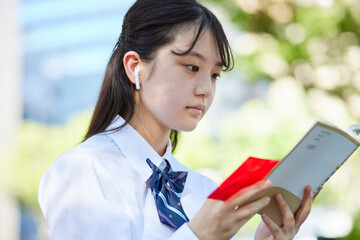 Fototapeta premium 屋外で参考書で勉強をする女子高校生