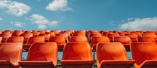 Close-up shot of empty orange stadium seats against a blue sky backdrop, providing ample copy space image.