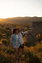 A couple exploring a scenic area at sunset, with the man pointing towards a distant point of interest.  The warm sunlight bathes the landscape, theme of travel, nature, and discovery.