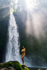 Woman in Yellow Swimsuit Looking Up at Sunlight by Waterfall