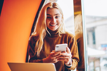 Portrait of cheerful hipster girl celebrating victory in online contest get email on smartphone,...