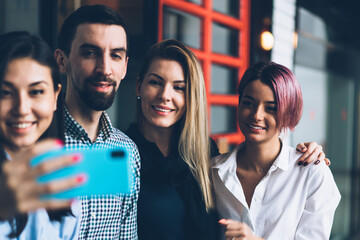 Young positive skilled group of employees having fun while taking together photo on smartphone camera for sharing in social network.Prosperous crew enjoying working break and making selfie on cellular