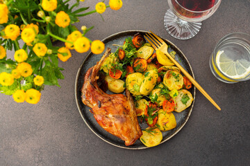 A hearty delicious dinner, baked rabbit with potatoes and carrots, a set table with food, a glass of wine and a vase of flowers