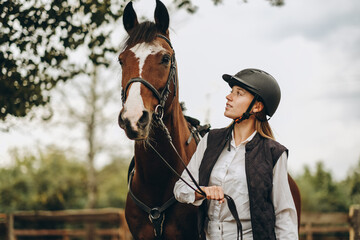 A young female equestrian stands near her horse and prepares for a competition.
