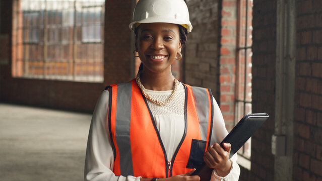Confident Female Engineer on Construction Site Holding Tablet and Wearing Safety Gear