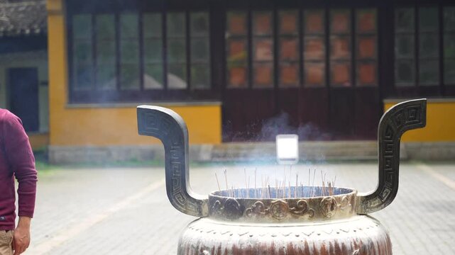 Man near garge incense burner in Chinese temple courtyard. Suzhou, China