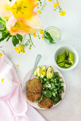 Quinoa cutlets and mixed salad with avocado and radishes, kiwi and water with lemon, delicious hearty breakfasts, a set table with food and a vase of flowers, vegan lunch plate