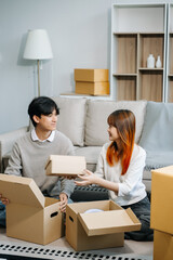 Young couple with big boxes moving into a new house, new apartment for couple, young asian man and woman helping to lift boxes on sofa for