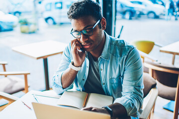 Mature handsome creative businessman in eyeglasses communicating with partner and discussing startup via cellphone.Good looking architect talking with friends on smartphone during sitting indoors