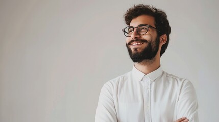 Fototapeta premium Confident bearded man in glasses smiling while looking to the side with arms crossed in white shirt against a neutral background.