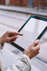 Cropped view of young woman's hands touching mock up display of modern tablet device with 4G internet.Hipster girl choosing app for download on touch pad with blank screen area for website content