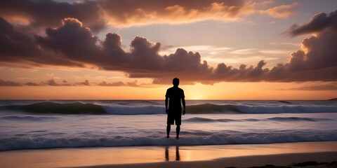 Fototapeta premium A silhouette of an isolated person standing on a beach at sunset, with waves crashing and a beautiful sky with clouds in the background