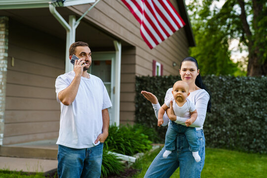Young pretty family standing in front of house outdoors. Father talk phone and bother mother