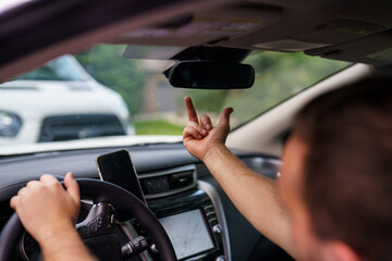 Handsome man at the wheel shows an indecent gesture