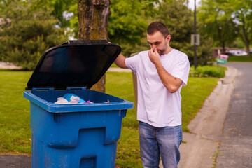 Young man show the bad smell emanating inside a large plastic mobile trash bin.