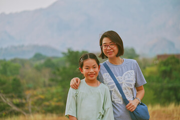 Portrait Asian middle-aged mother and little daughter together on a hill in the morning. Healthy middle-aged woman and child on vacation, space for text, landscape image.