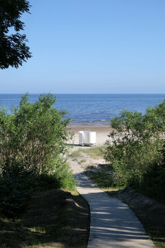 Wooden walkway leads down through plant covered dunes to sandy beach and the Baltic sea in Jurmala, Latvia. A white changing pod can be seen in the middle of the frame.